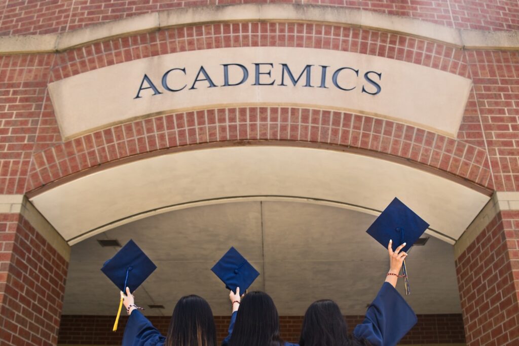 three girls in graduation gowns hold their caps in the air